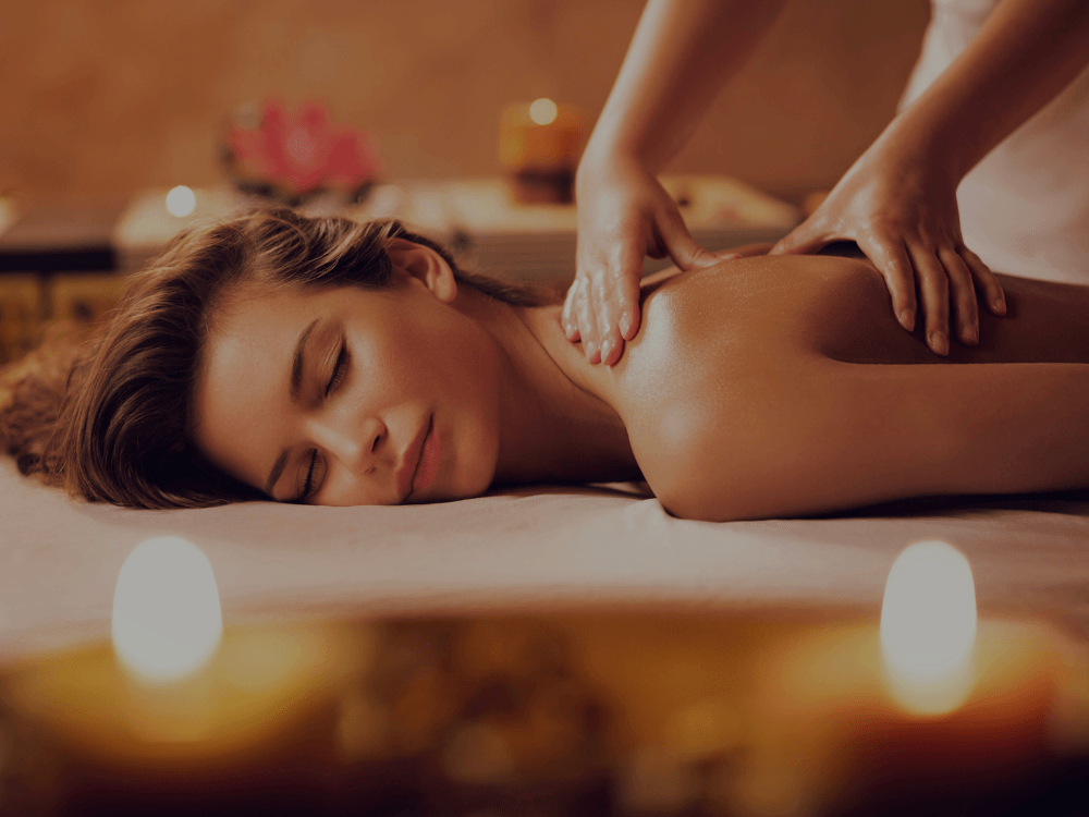 Frau liegt entspannt auf einer Massageliege und erhält eine Rückenmassage bei Kerzenschein.