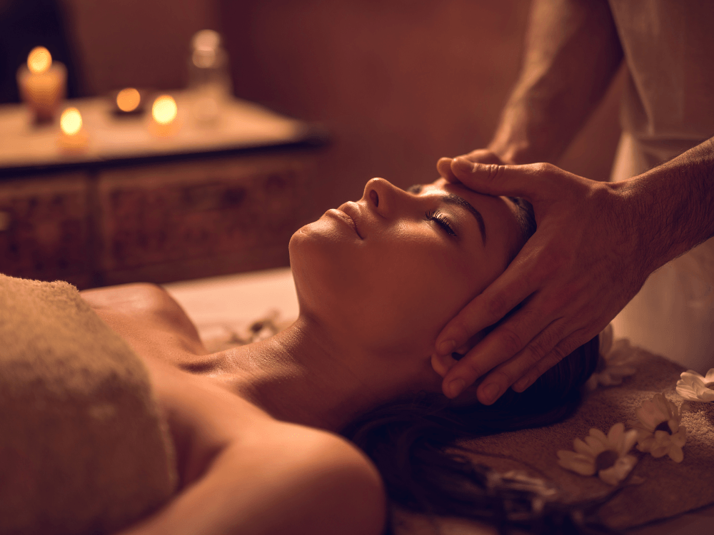 Frau liegt entspannt im Spa und erhält eine Stirnmassage bei gedämpftem Kerzenlicht.