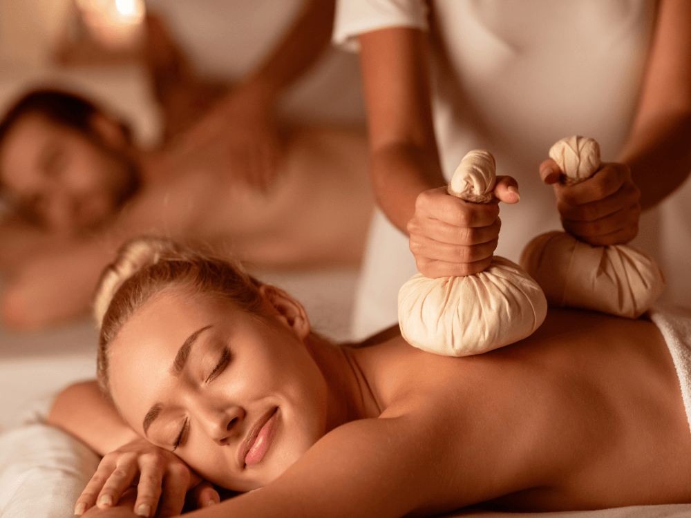 Zwei Personen erhalten parallel eine Kräuterstempelmassage – entspannte Atmosphäre in einem Wellnessraum.