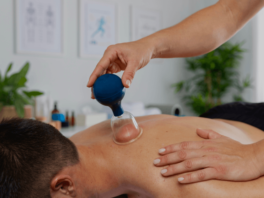 Schröpfmassage mit Glas-Schröpfkopf und Vakuumball auf dem Rücken eines liegenden Mannes.