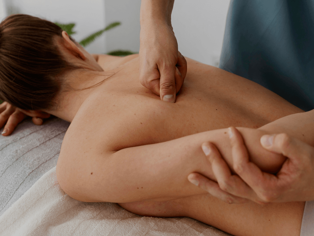 Rückenmassage: Therapeutin übt mit Daumen gezielten Druck auf den Rücken einer liegenden Frau aus.