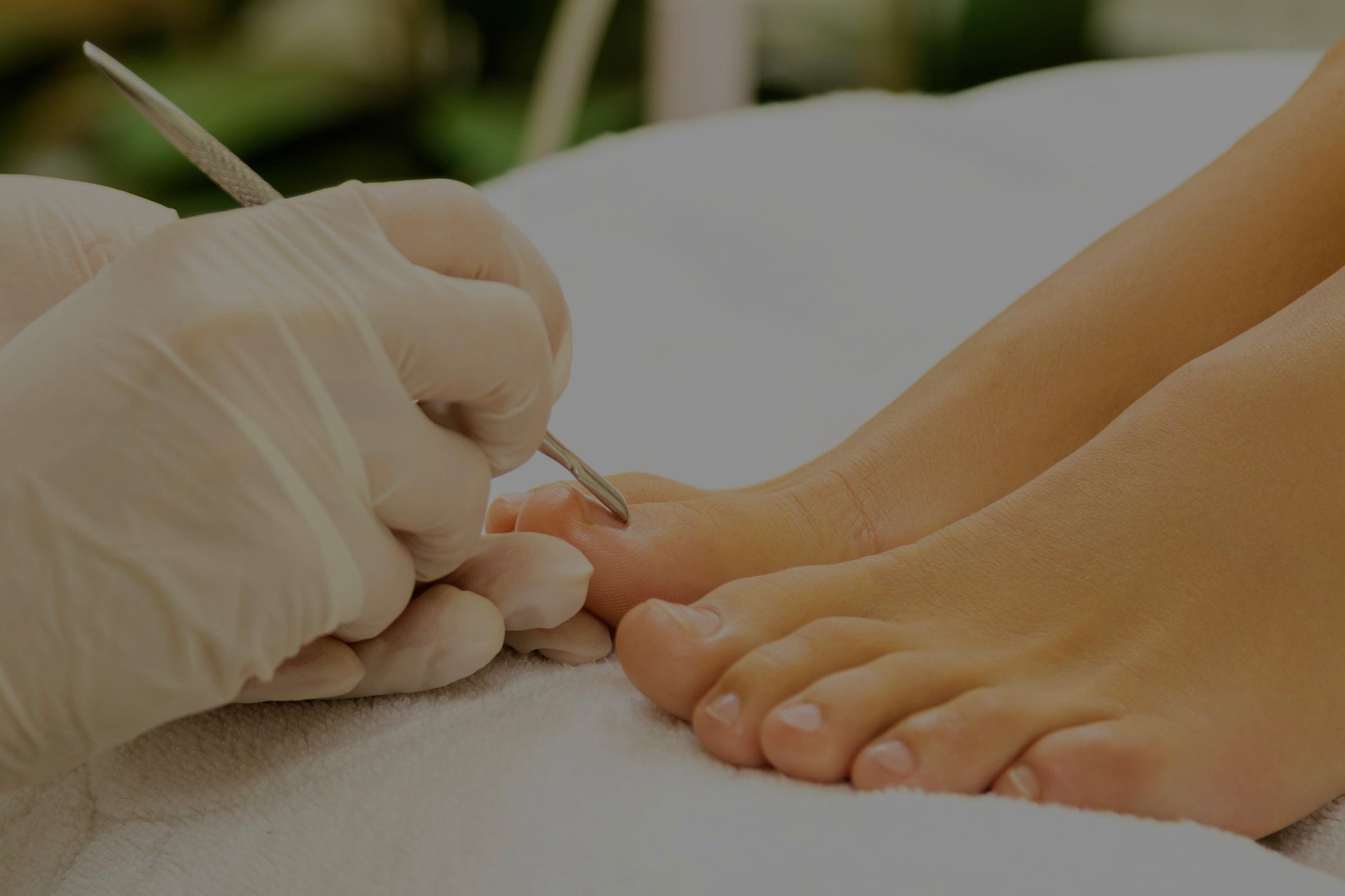 Nahaufnahme einer professionellen Fußpflege – Behandlung mit Instrument am Zeh durch eine Person mit Handschuhen.