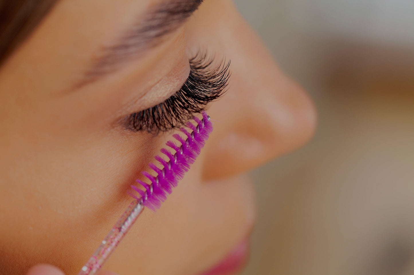 Nahaufnahme einer Frau, die ihre verlängerten Wimpern mit einer pinken Wimpernbürste kämmt.