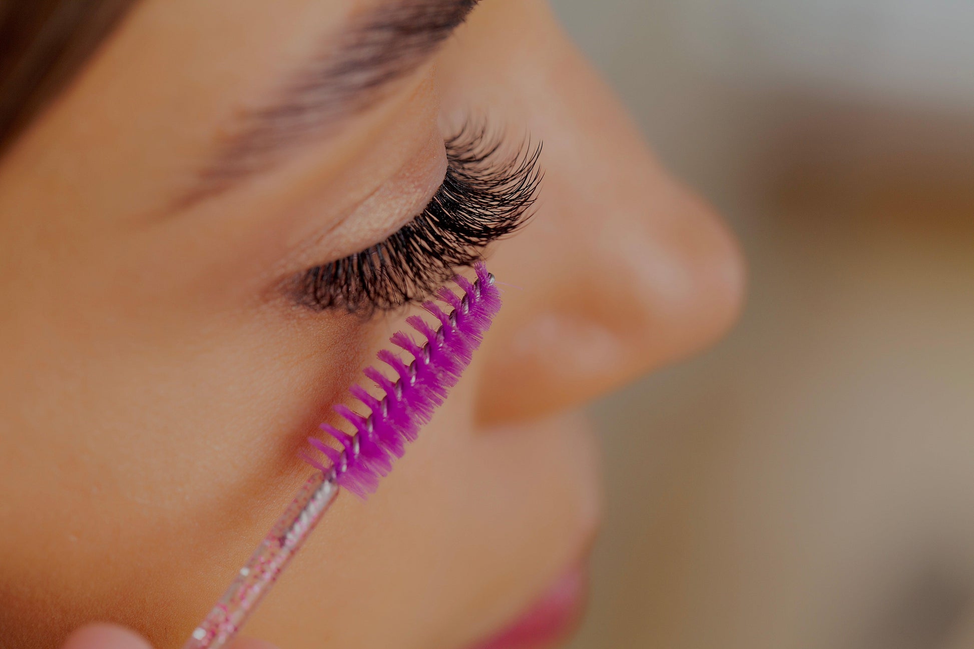 Nahaufnahme einer Frau, die ihre verlängerten Wimpern mit einer pinken Wimpernbürste kämmt.